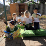 children sitting on some decking reading outside